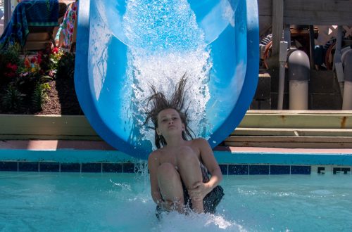 boy sliding off blue water slide into pool