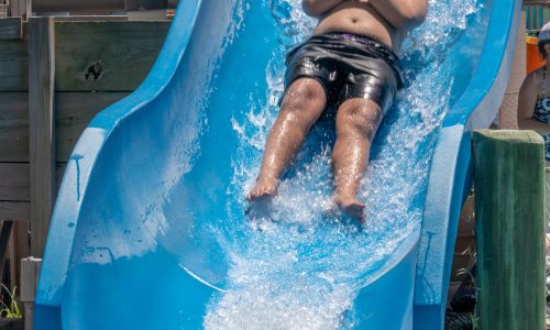 Boy with arms crossed sliding down blue water slide