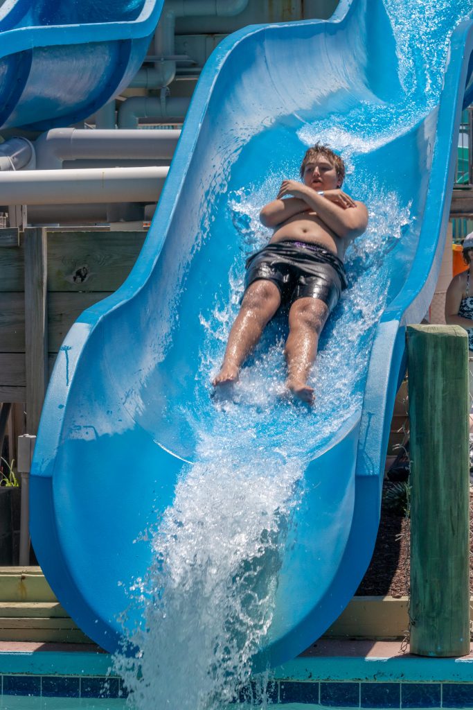 Boy with arms crossed sliding down blue water slide